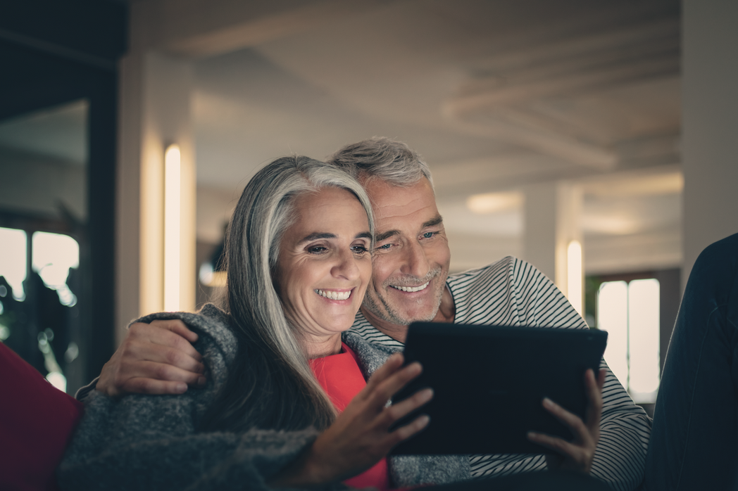 Ein älteres Paar schaut lächelnd gemeinsam auf die Inhalte am Bildschirm des Tablets