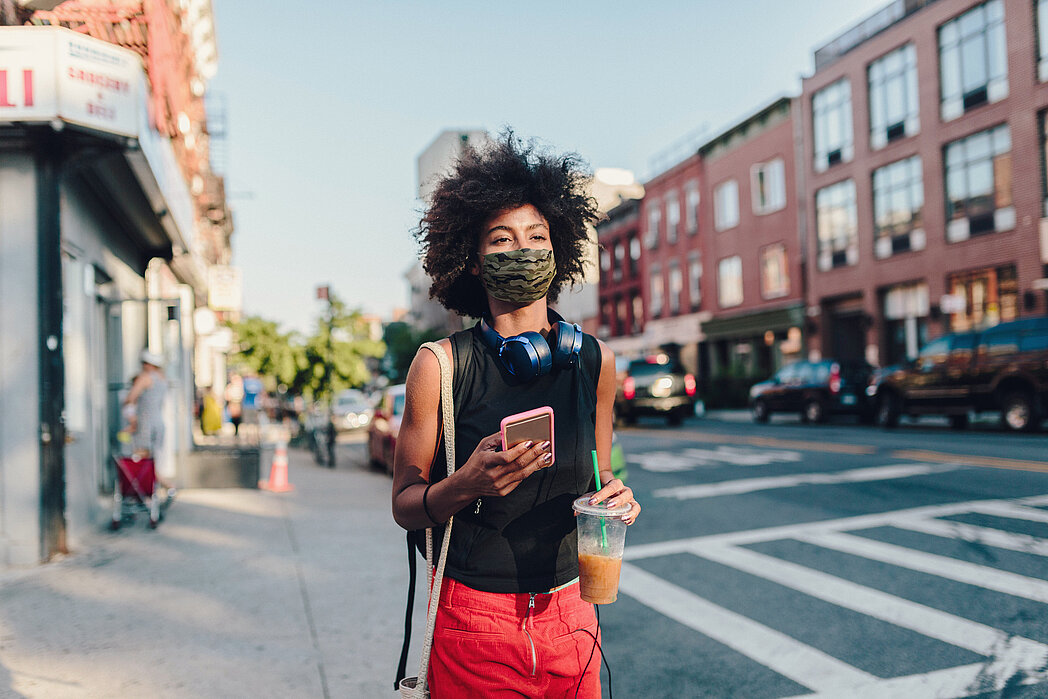 Frau mit Mund-Nasen-Bedeckung und Smartphone