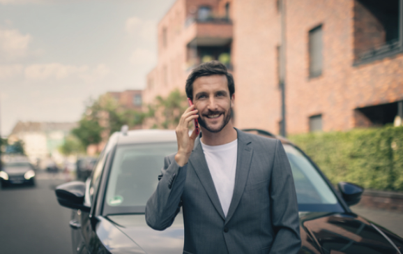 Mann telefoniert vor seinem Auto und lacht